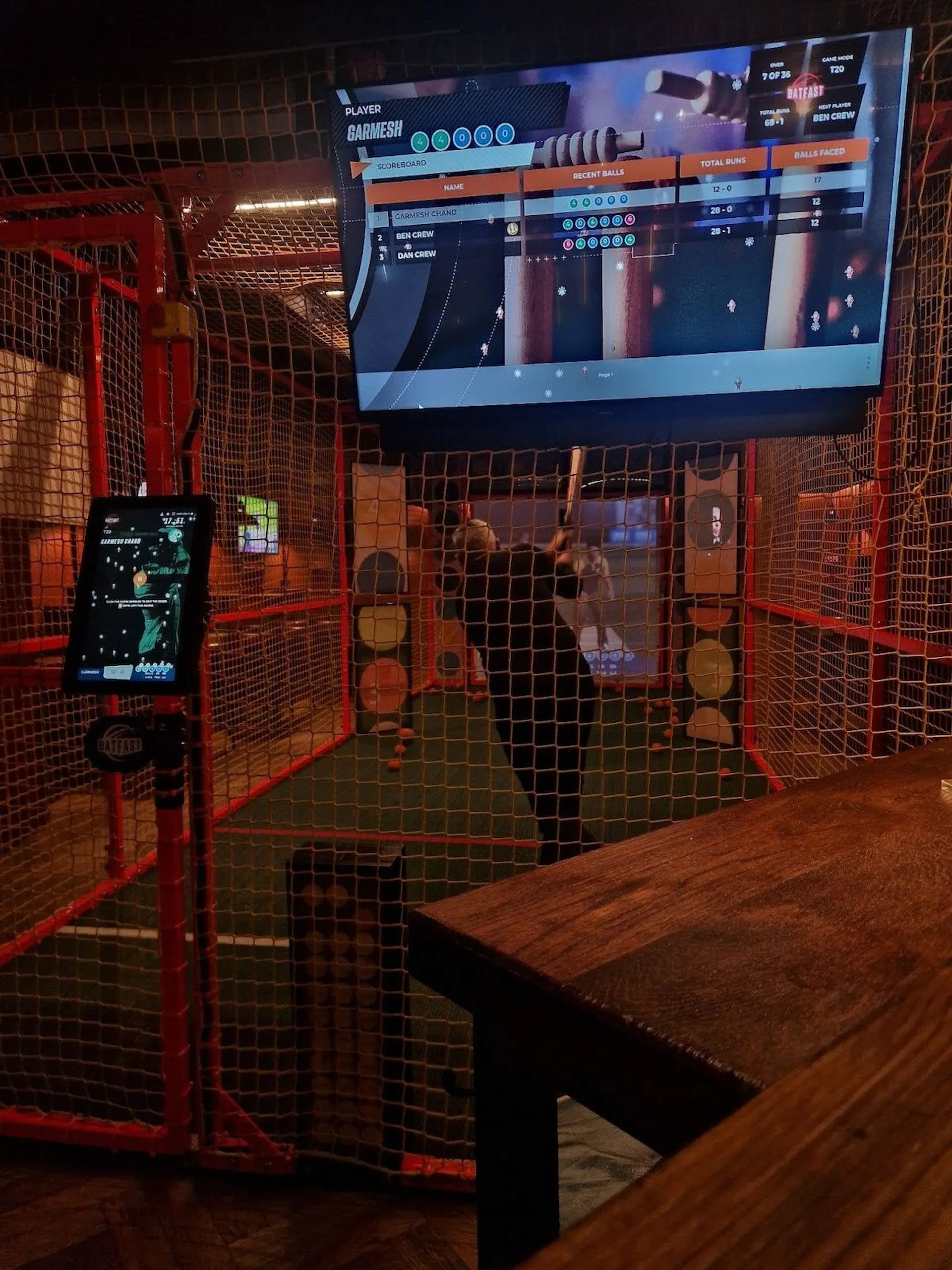 GC Reports team-building event: An engineer at the batting crease of an interactive cricket simulator with a digital scoreboard