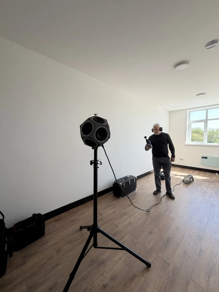 Sound Insulation Testing in Wigan by GC Reports. The image shows a professional acoustic engineer using a dodecahedron power speaker and a sound level meter to test a residential property for Part E building regulation compliance.